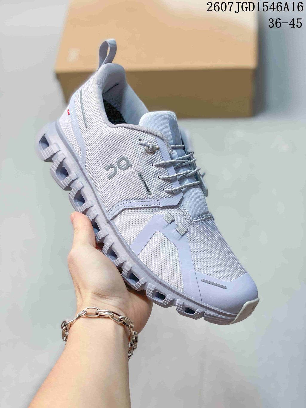 Angled side view of the light gray sneaker showing the lace-up upper, side branding, heel pull tab and segmented outsole.