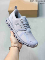 Angled side view of the light gray sneaker showing the lace-up upper, side branding, heel pull tab and segmented outsole.