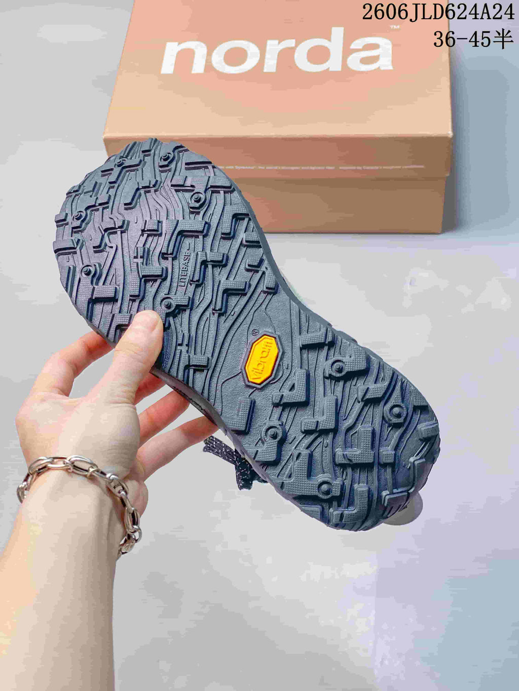 Close-up of the hiking shoe's lugged outsole, with Norda packaging in the background.