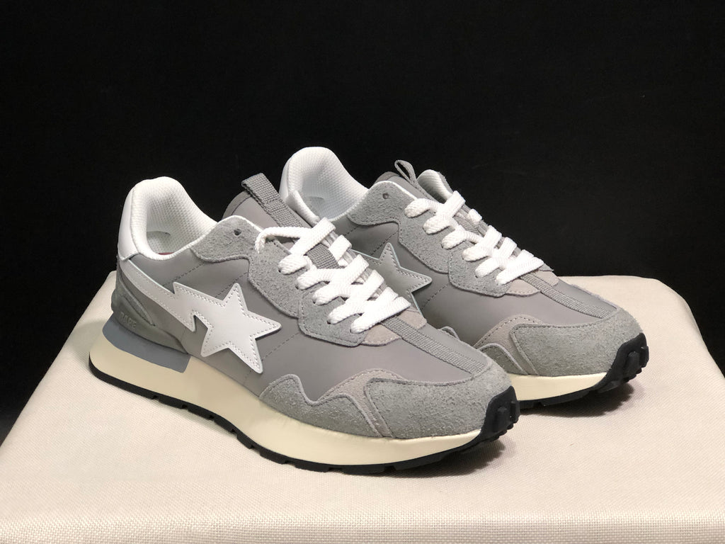 Front three-quarter view of the pair showing grey textured overlays, white laces, white star emblems, and cream midsoles.