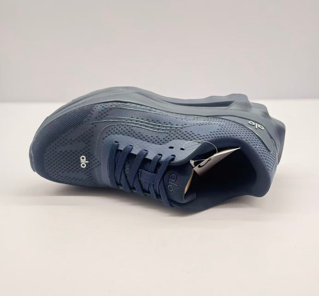 Top view of one dark blue Alo sneaker highlighting the lace arrangement, tongue branding, and perforated-looking upper pattern.