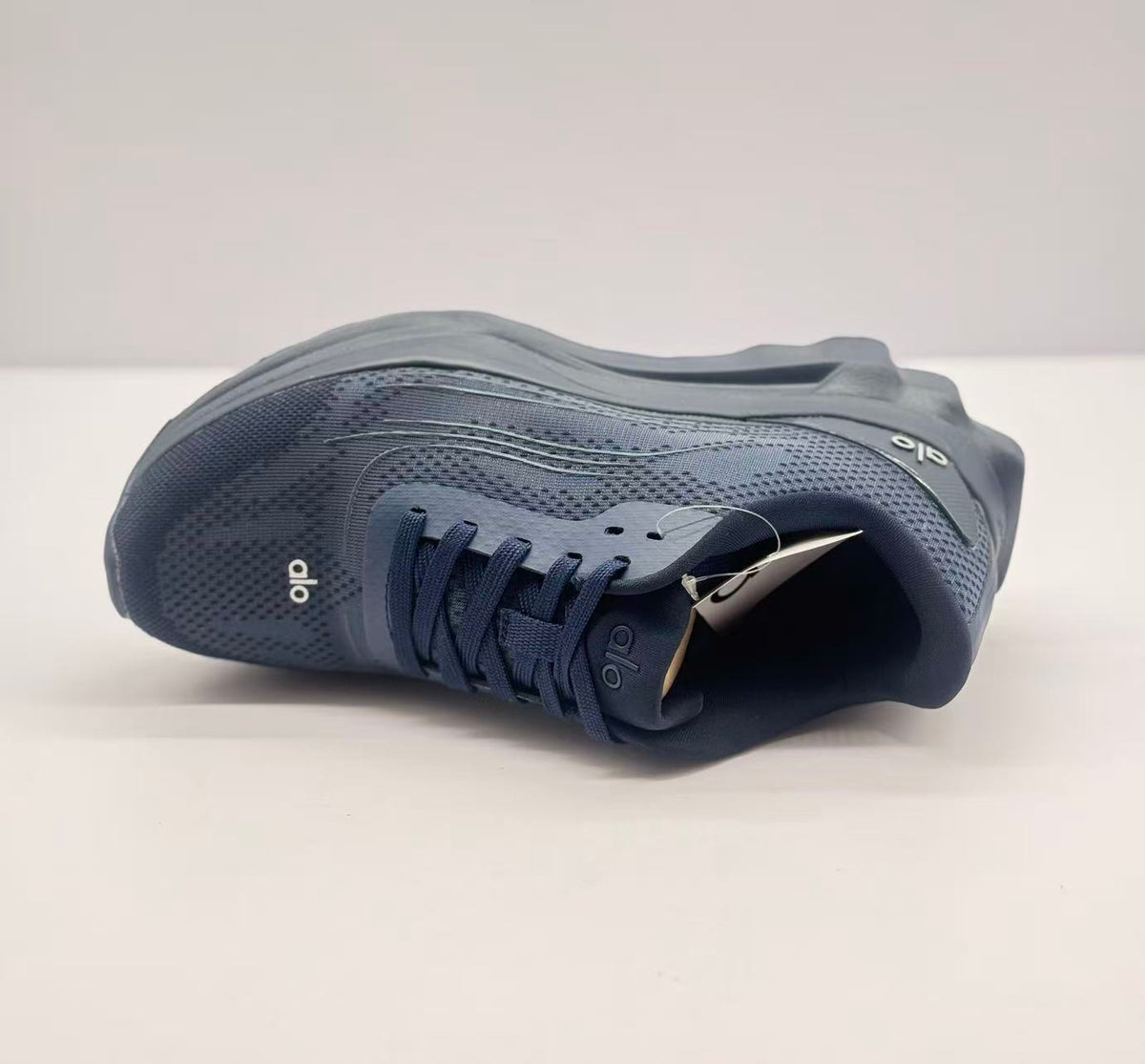 Top view of one dark blue Alo sneaker highlighting the lace arrangement, tongue branding, and perforated-looking upper pattern.