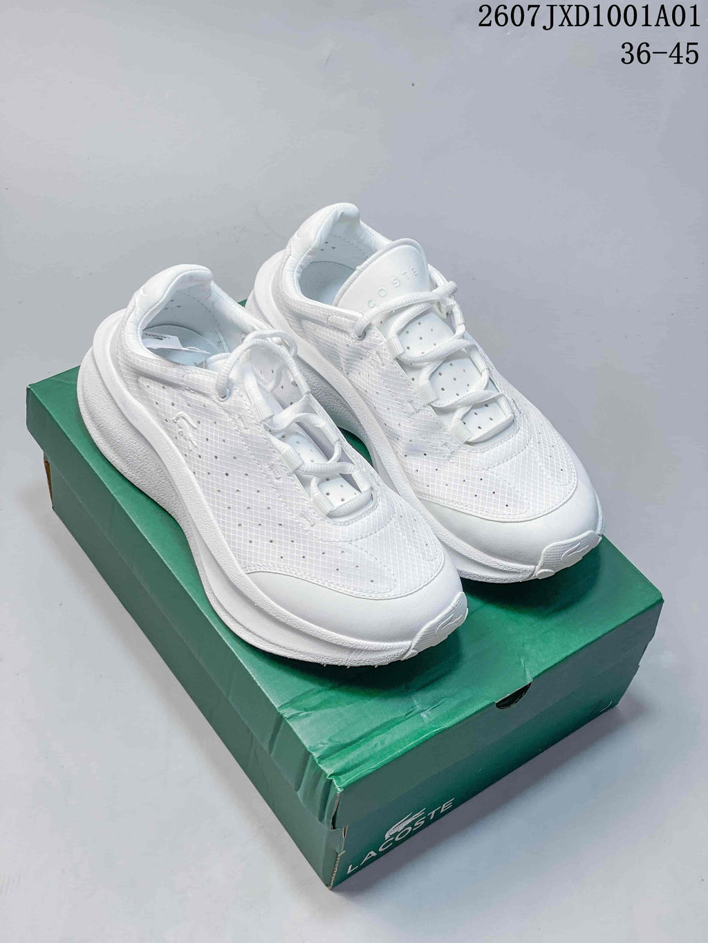 Pair of white Lacoste lace-up sneakers shown on a green shoe box