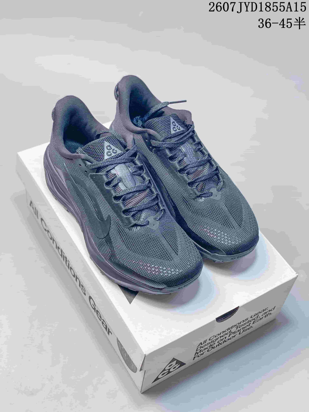 Pair of dark gray Nike ACG Pegasus Trail sneakers displayed on a shoebox, showing the woven-look uppers, lace-up design, and lugged soles.