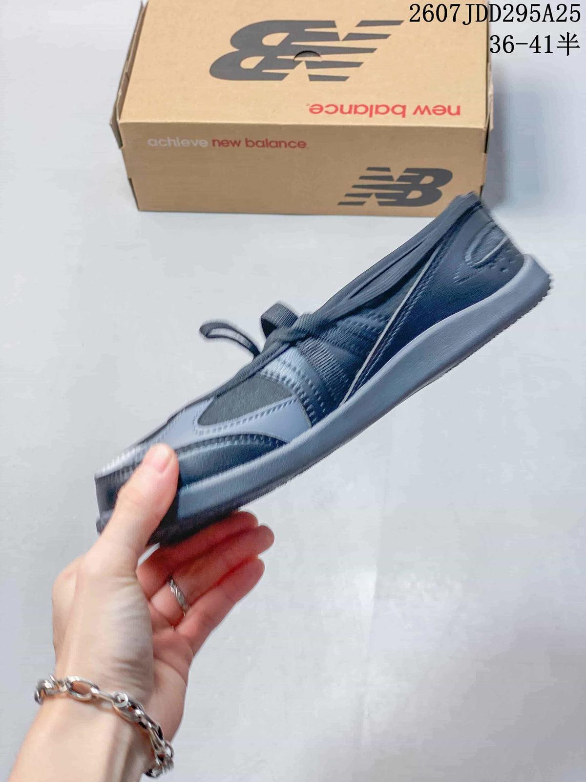 Side profile showing the low-profile silhouette, layered black and gray upper, strap, laces, and slim gray outsole.