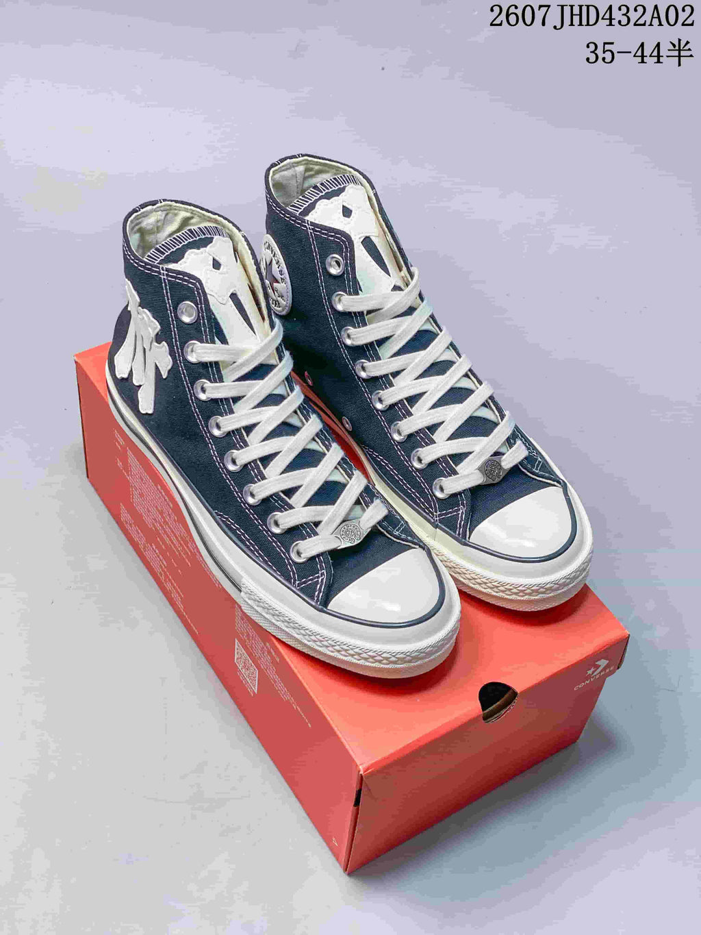Pair of navy high-top Converse-style sneakers with white laces and decorative patches on a red shoebox