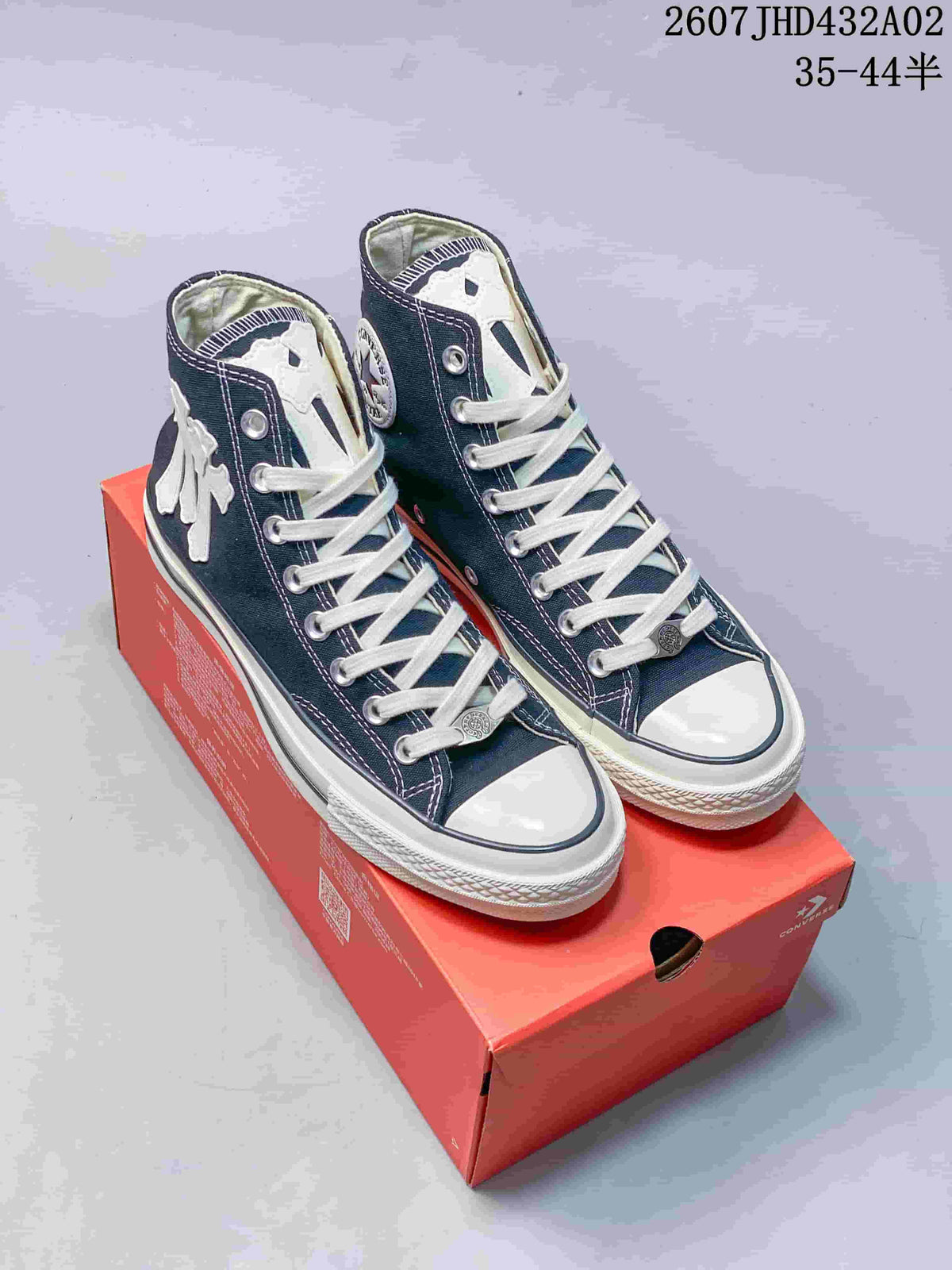 Pair of navy high-top Converse-style sneakers with white laces and decorative patches on a red shoebox