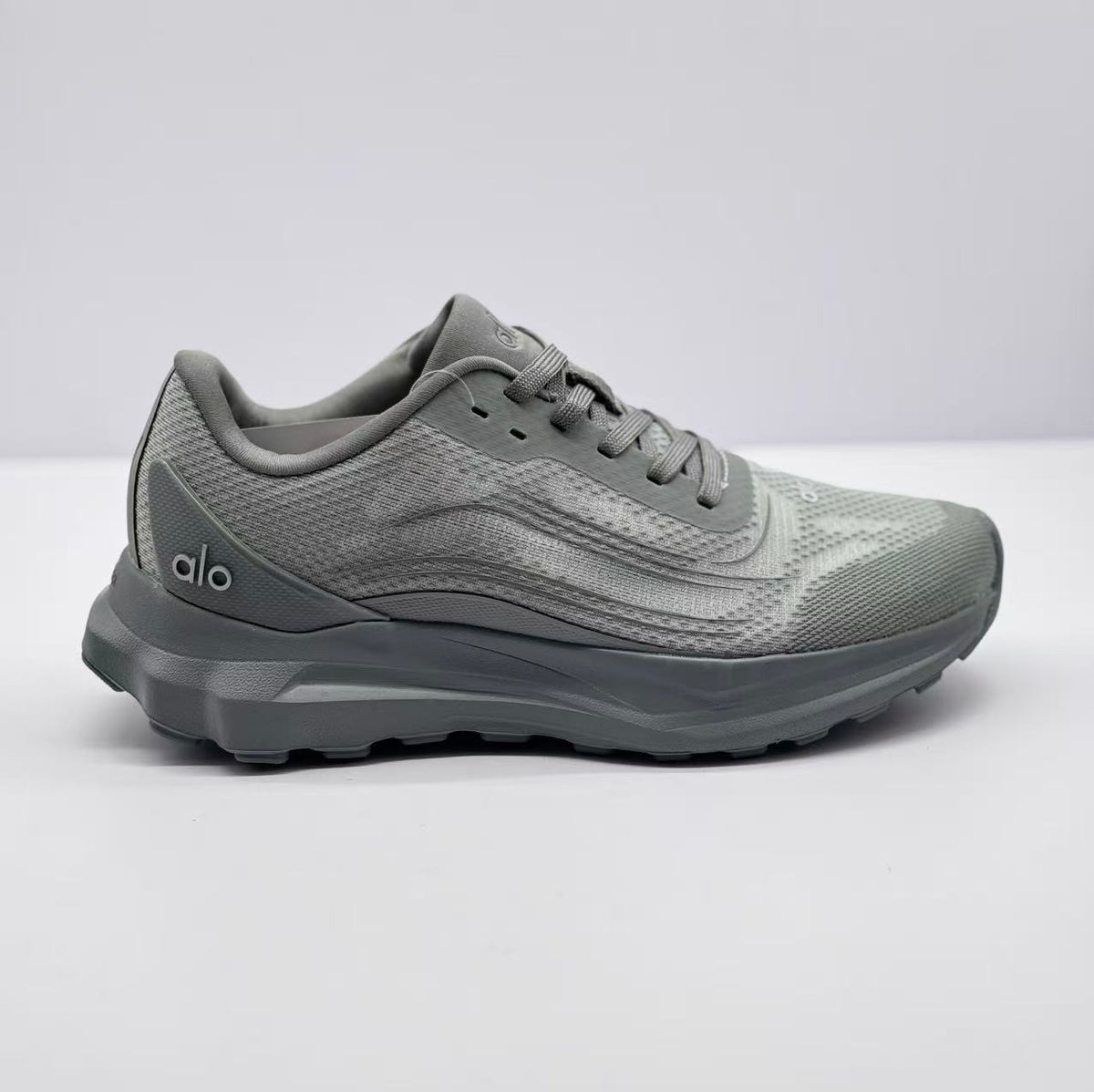 Side view of a gray Alo Runner sneaker showing the lace-up upper, layered side detailing, padded collar, and thick outsole.