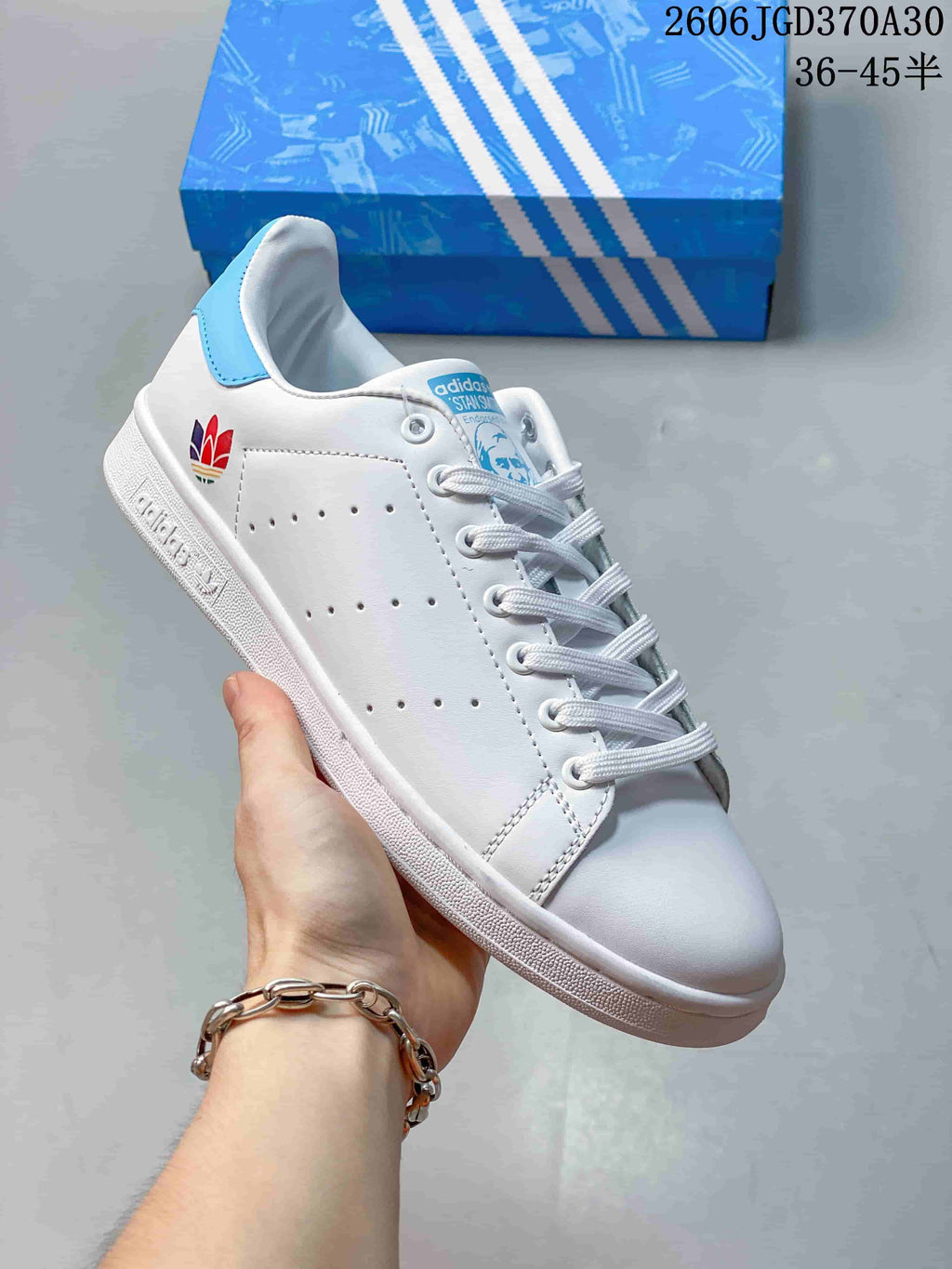 White Stan Smith-style sneaker with a multicolor heel emblem and a light-blue heel tab.
