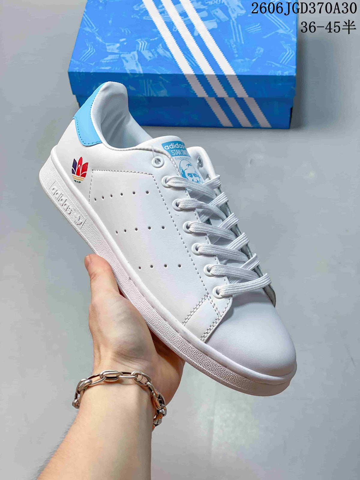 White Stan Smith-style sneaker with a multicolor heel emblem and a light-blue heel tab.