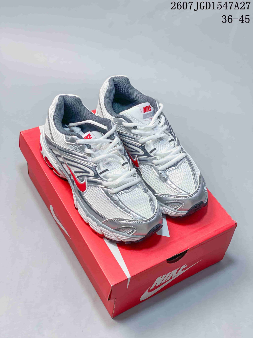 Pair of Nike Air Max Moto 2K sneakers on a red shoebox, showing the white and silver upper with red accents.