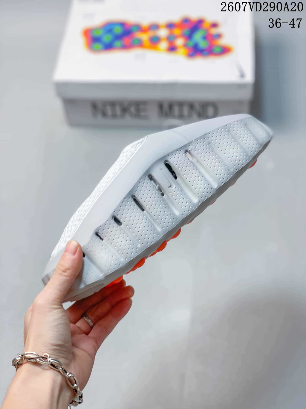 Side and outsole view showing the perforated light gray upper, sculpted sole, and orange outsole elements.