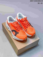 Pair of orange ON Cloudmonster 3 Hyper sneakers displayed on a cardboard box, with white midsoles and black details.