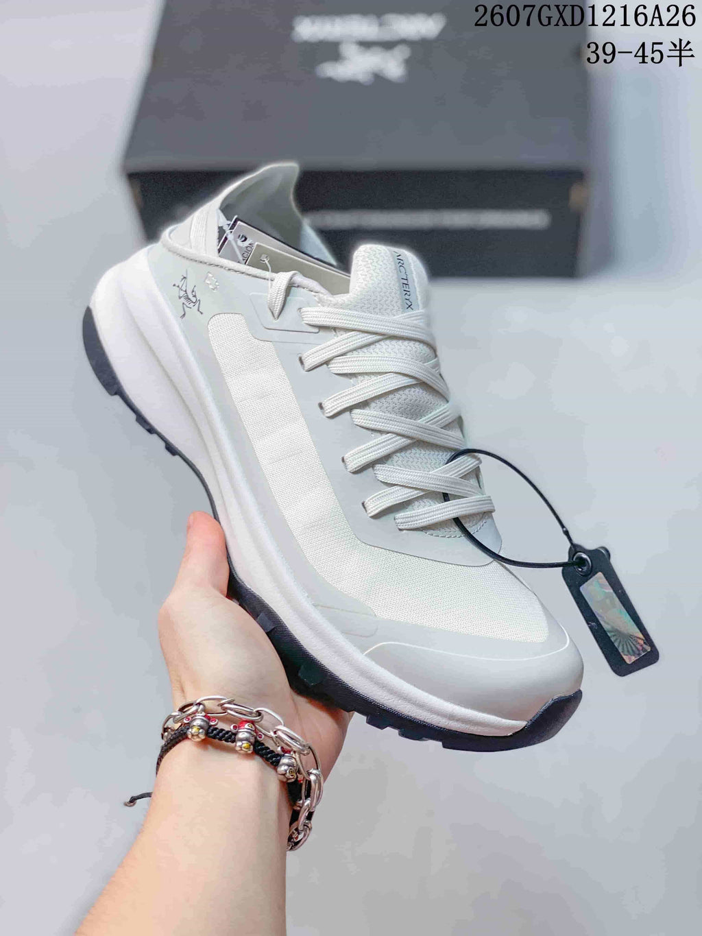 Angled side view of the white Arc'teryx sneaker with its layered upper, heel pull area, laces and attached tag.