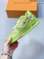 Side view of the green low-top sneaker showing the textured upper, outlined panels, multicolor motifs, and pink trim.