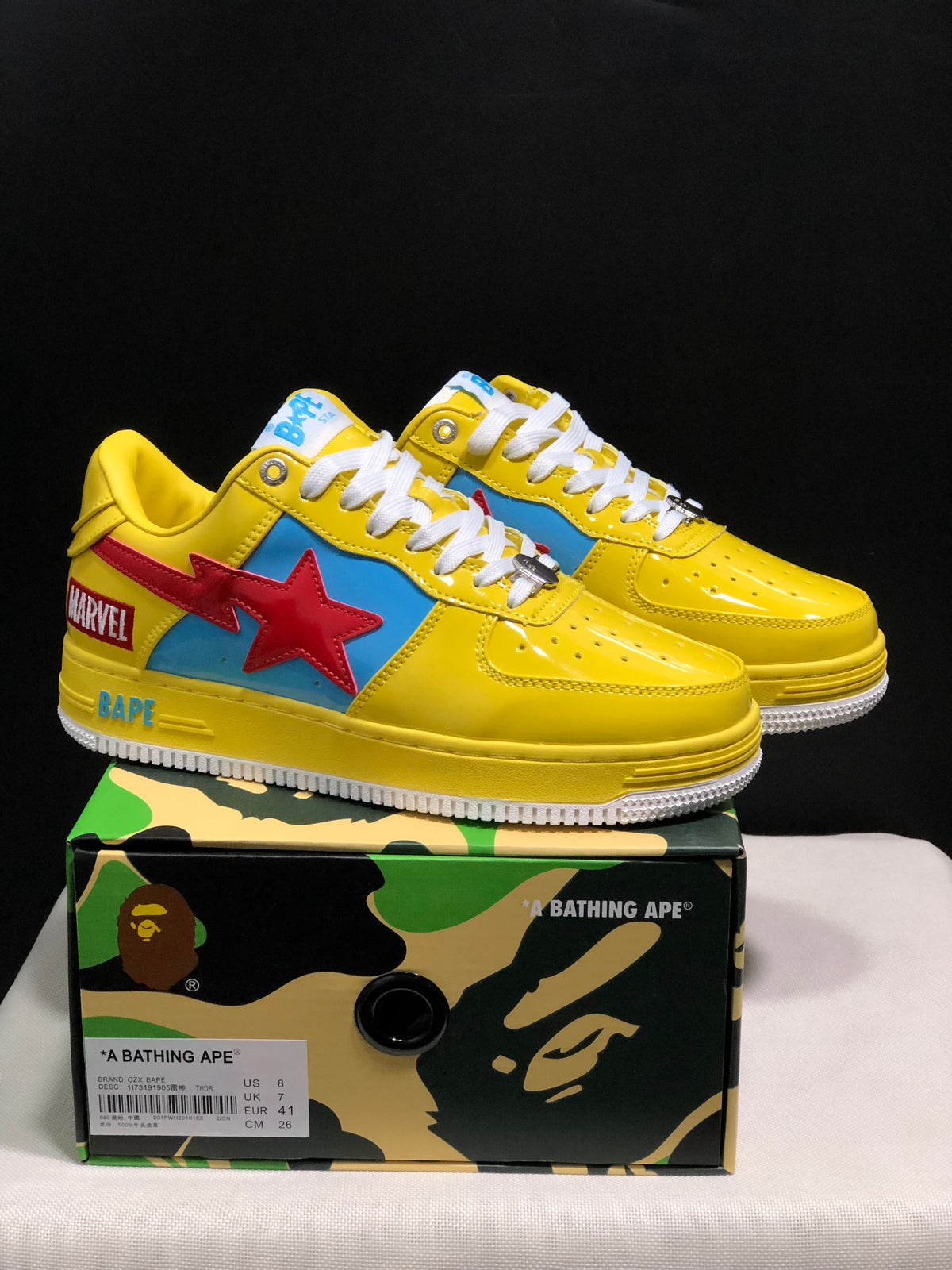 Pair of yellow BAPE low-top sneakers with blue panels, red star graphics, white laces, and a product box; the box label shows EU 41 and CM 26.