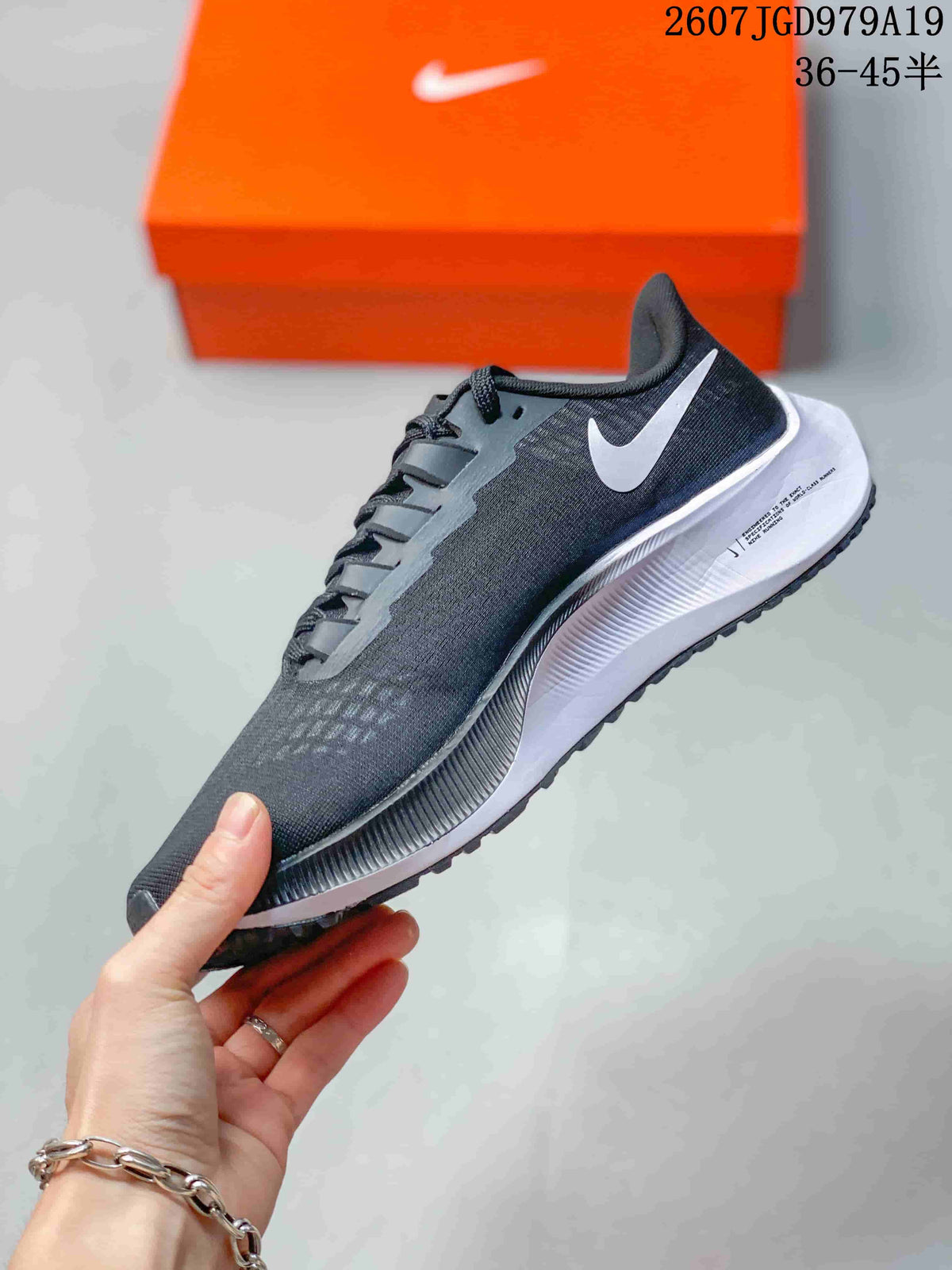 Side profile of the dark Nike Pegasus 37 sneaker showing the contrasting side branding, textured upper, white midsole, and black outsole.