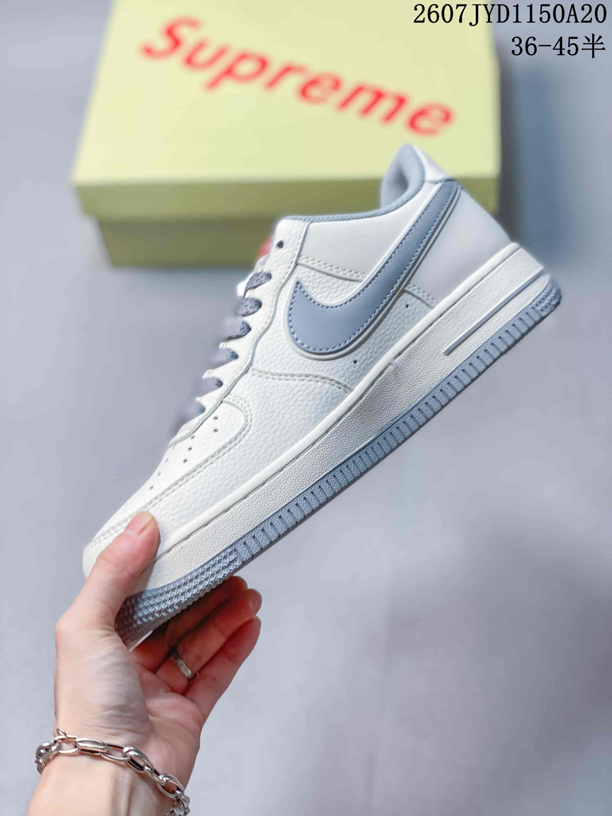 Side view of the white low-top sneaker with a grey Swoosh, layered panels, white midsole, and grey outsole.