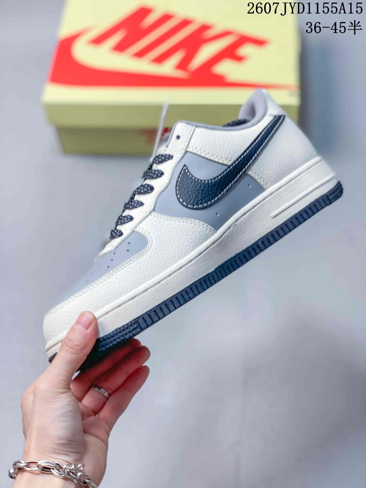 Side view of the Nike Air Force 1 sneaker showing the grey side panel, navy Swoosh, white upper sections and white midsole.