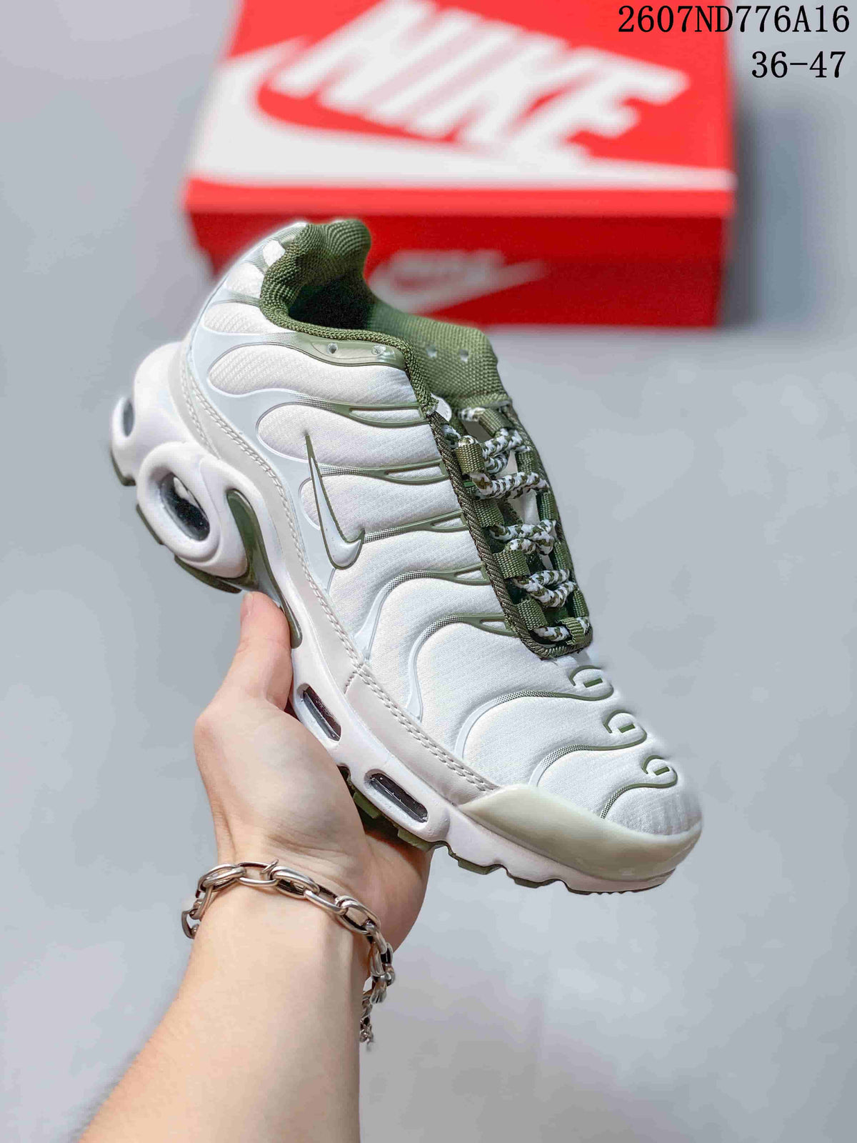 Angled side view of the white and green Nike Air Max Plus sneaker showing layered upper panels, side branding, and air units.