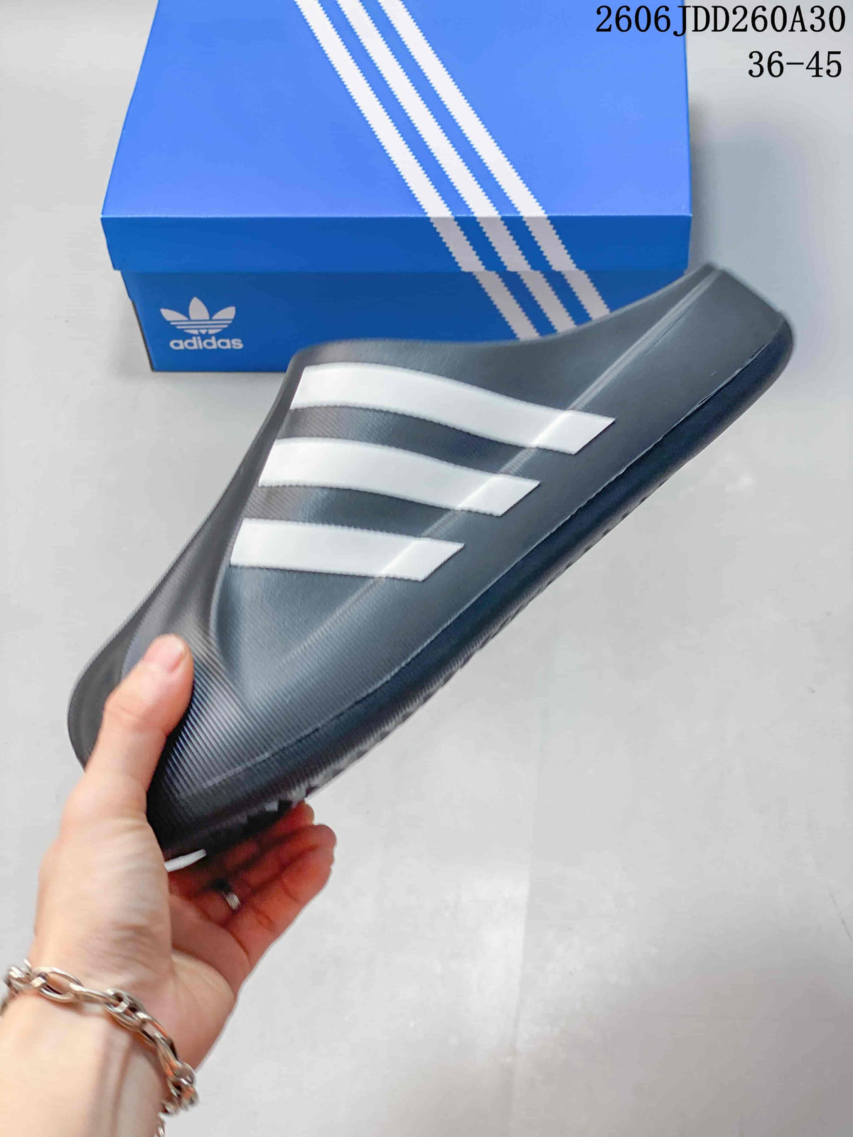 Side profile of a charcoal closed-toe mule slide with three white stripes