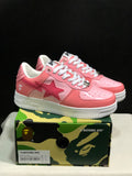Pink and white BAPE Sta sneakers displayed on a camouflage BAPE shoe box; the box label shows EU 41 and CM 26.