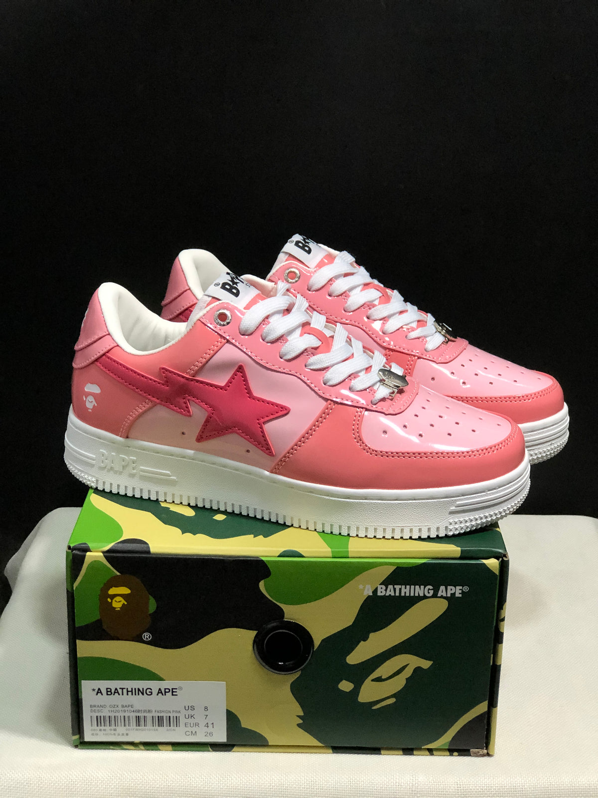 Pink and white BAPE Sta sneakers displayed on a camouflage BAPE shoe box; the box label shows EU 41 and CM 26.