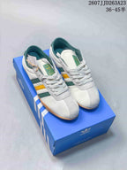Pair of white adidas Originals Tokyo sneakers with green and yellow stripes displayed on a blue adidas shoe box.