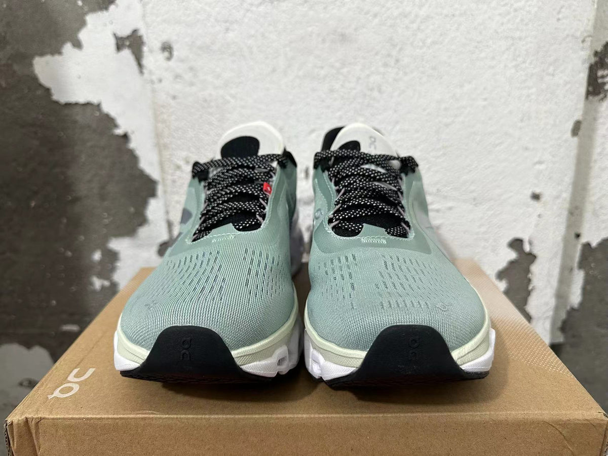 Front view of sage-green running shoes with black dotted laces and white soles.
