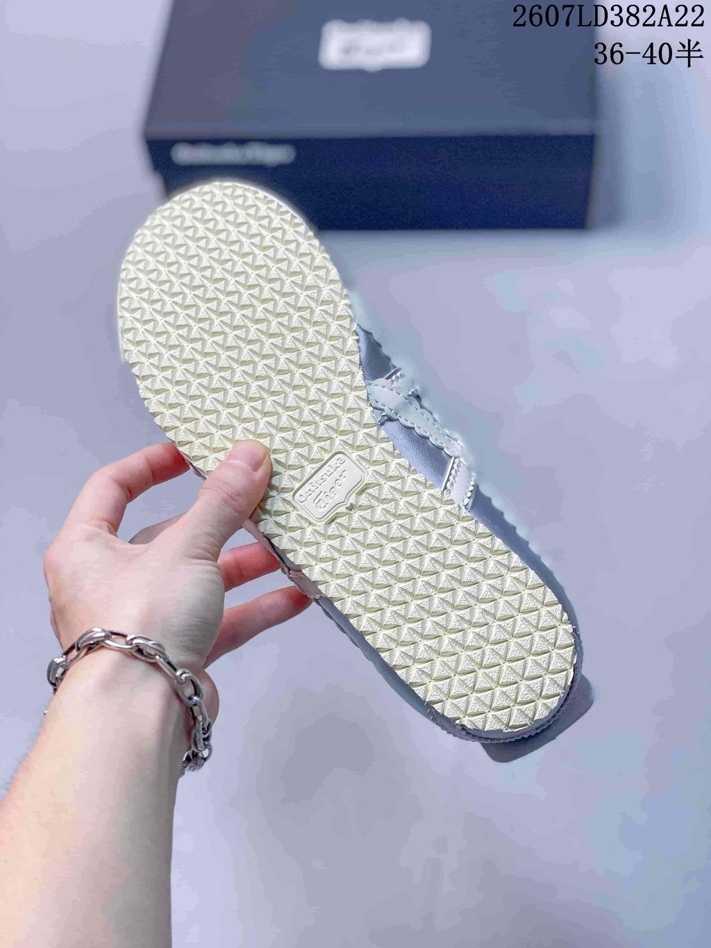 Underside view of the sneaker showing the repeating textured outsole pattern and source style code in the background.