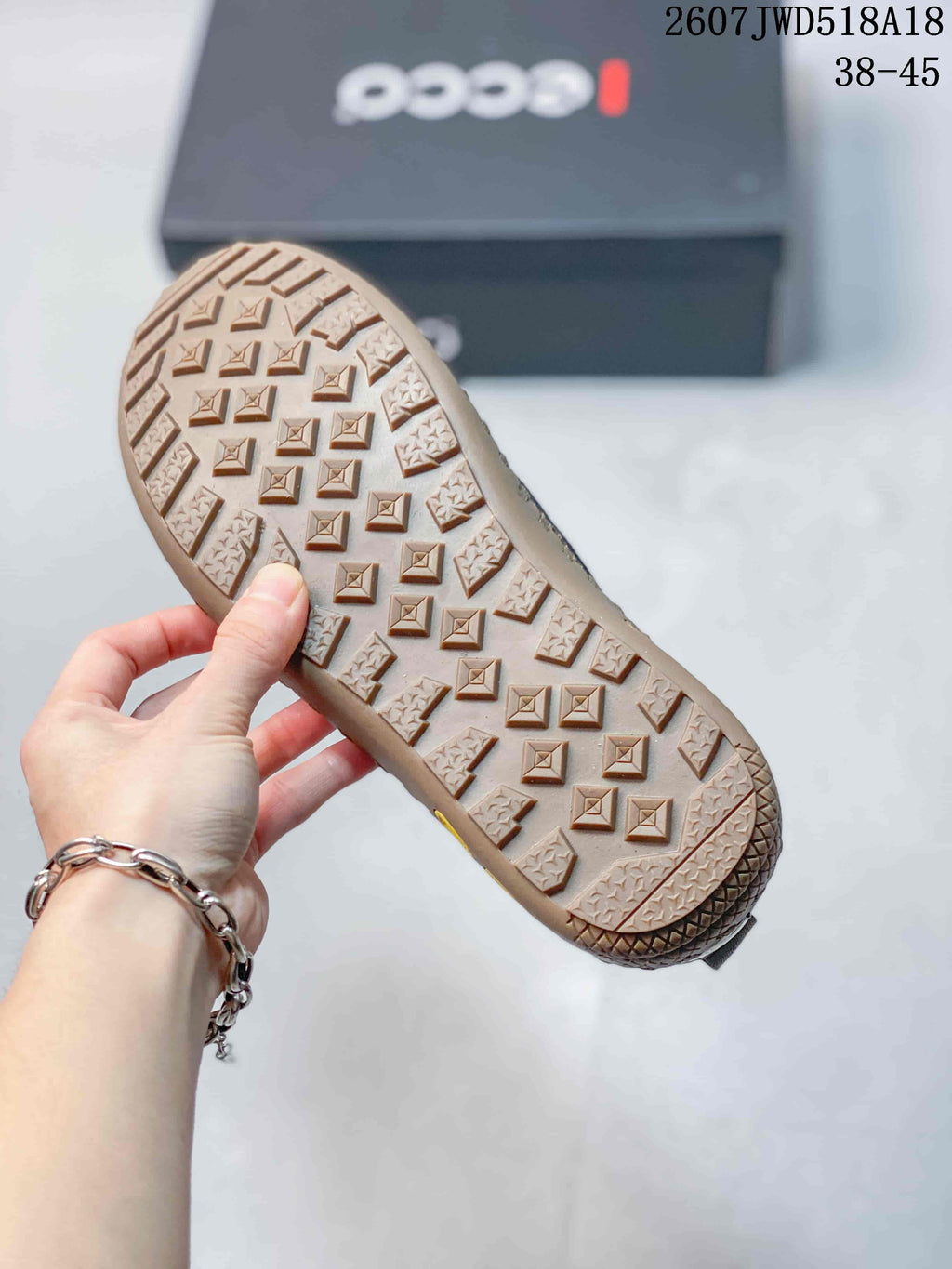 Close view of the tan patterned outsole showing raised geometric tread blocks; ECCO box and size range 38–45 appear in the background.
