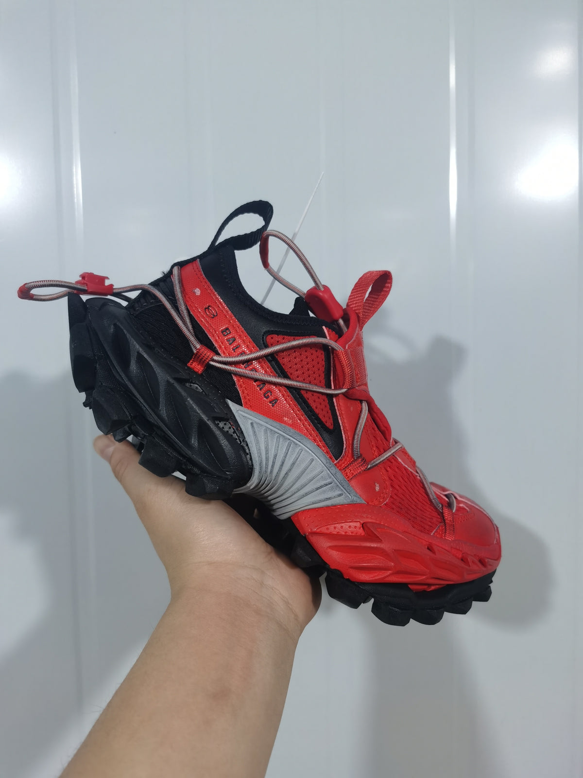 Angled front view of the red and black sneaker showing the textured toe, layered panels, looped lace system and black treaded outsole.