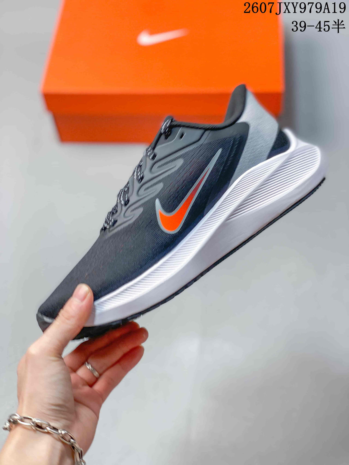 Side profile of the dark gray Nike running shoe with orange swoosh detail, white midsole, and low-top construction; image text shows style code 2607JXY979A19 and size range 39–45.