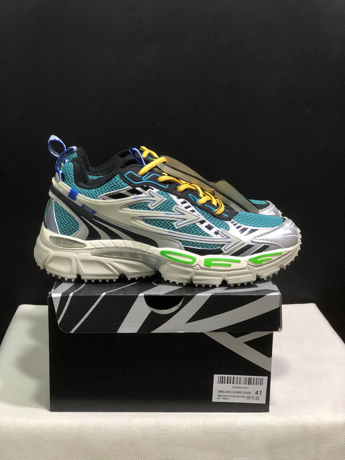 Side view of a teal mesh sneaker with layered white and black overlays, yellow laces, and a chunky off-white sole.