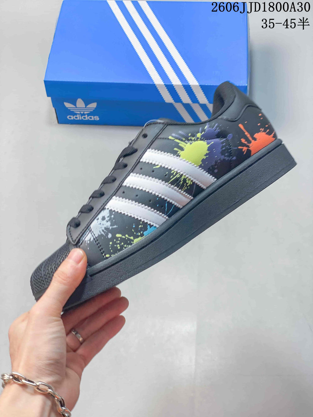 Side view of the black Superstar sneaker with white stripes, colorful splatter graphics, and a dark sole.