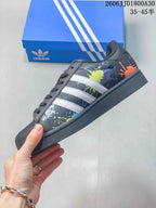 Side view of the black Superstar sneaker with white stripes, colorful splatter graphics, and a dark sole.
