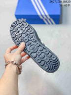 Close-up of the dark outsole showing circular tread elements and repeated Adidas trefoil details.