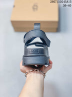 Rear view of a black sandal showing the heel strap, pull tab, raised sole, and UGG branding, with product code 2607JDD245A15 and size range 36–40 visible.