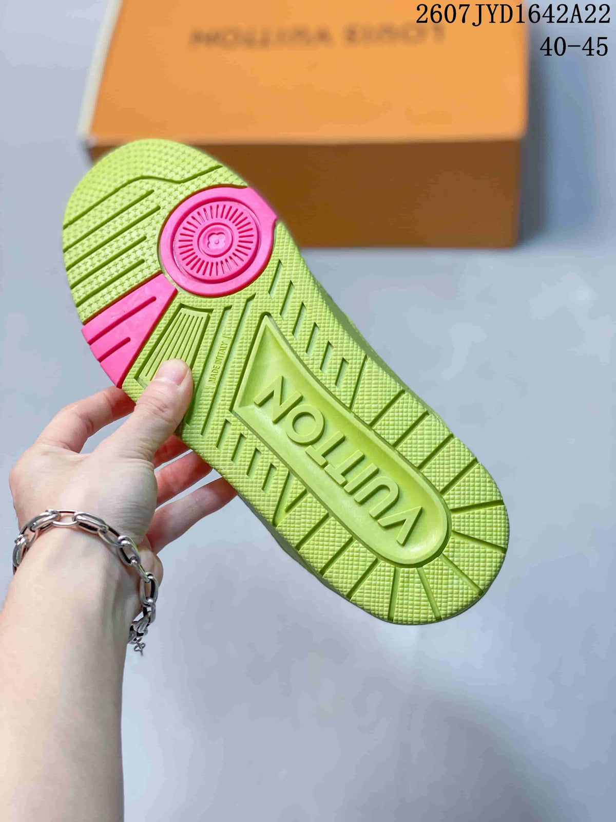 Underside of a green sneaker showing the textured rubber outsole, pink heel detail, and molded branding.