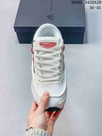 Front view of a white lace-up sneaker with mesh-like panels and coral-pink tongue detail