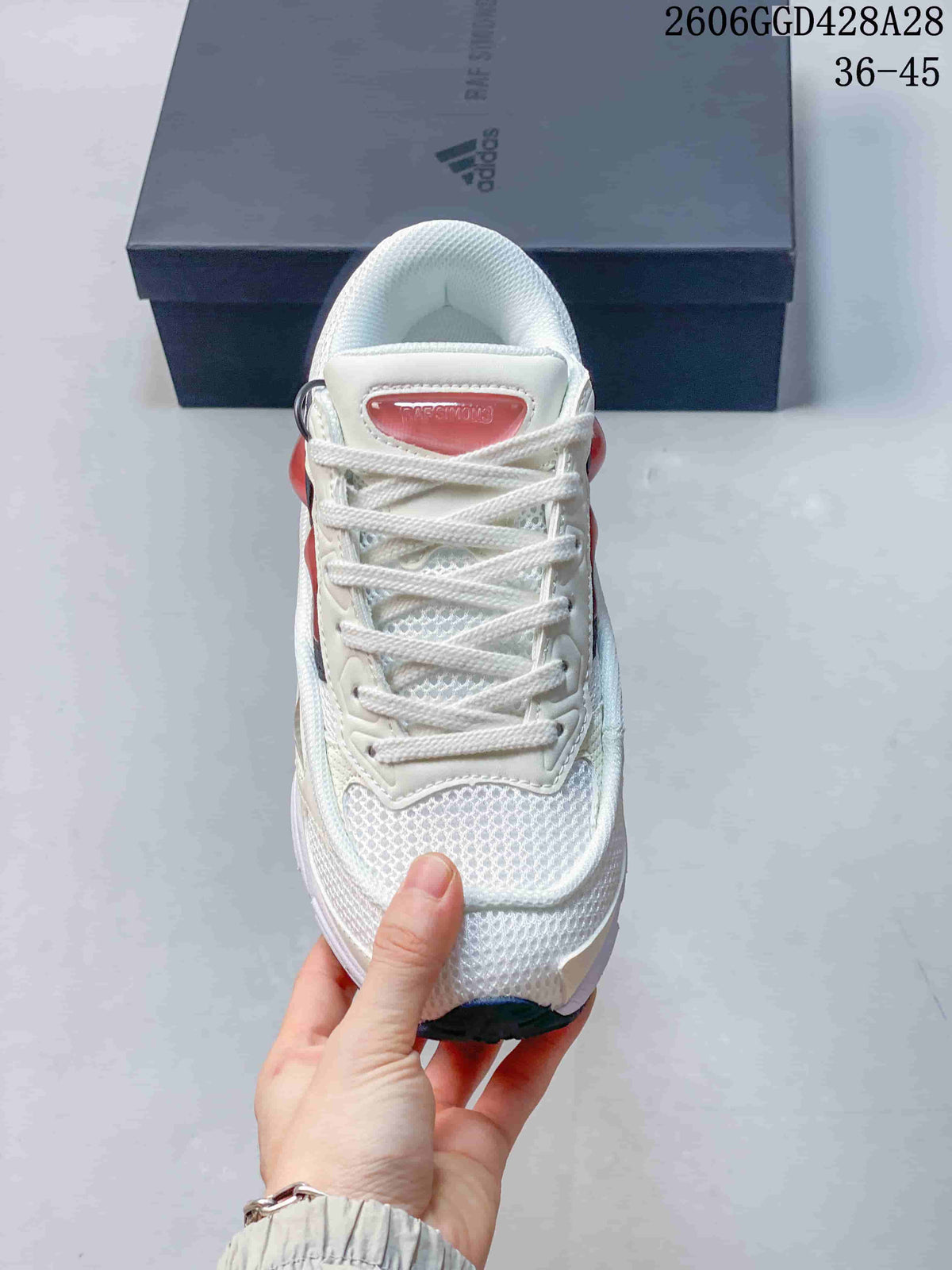 Front view of a white lace-up sneaker with mesh-like panels and coral-pink tongue detail