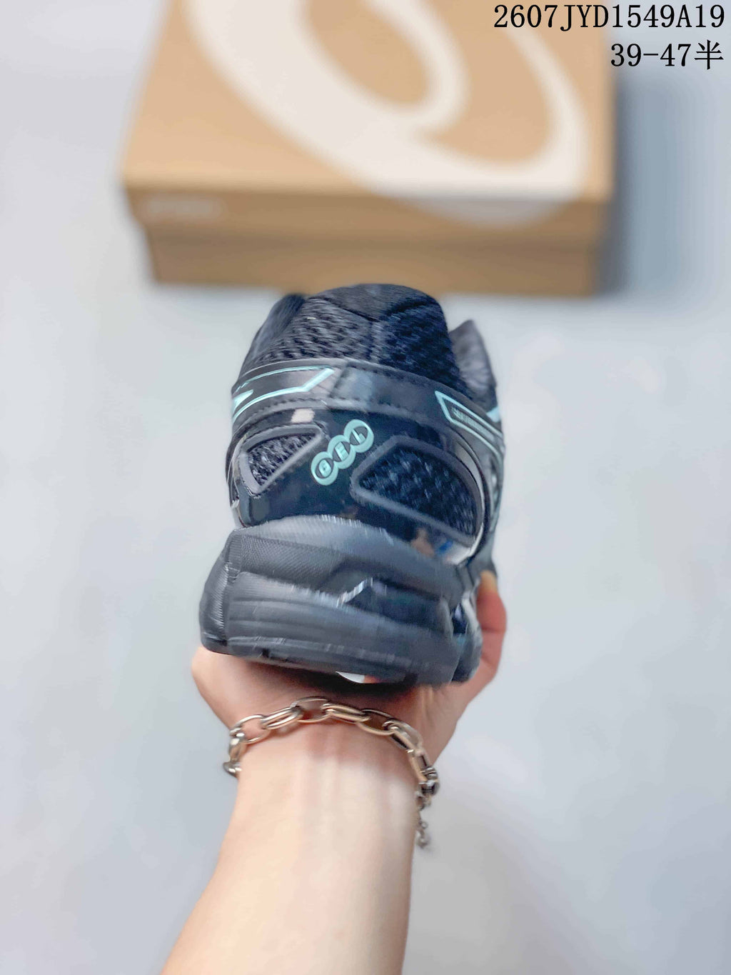 Rear view of a black and gray ASICS sneaker showing the padded heel area, heel branding, and layered sole construction; image text shows style code 2607JYD1549A19 and size range 39–47.5.