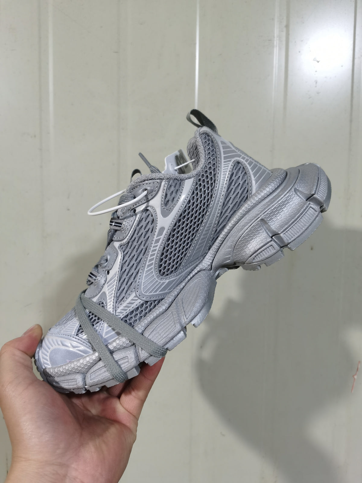 Close-up side view of a grey layered mesh sneaker with textured overlays, grey laces and a segmented sole.