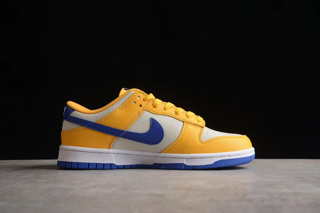 Side profile of the low-top sneaker showing the blue Swoosh, wheat gold overlays, white midsole, and blue outsole.