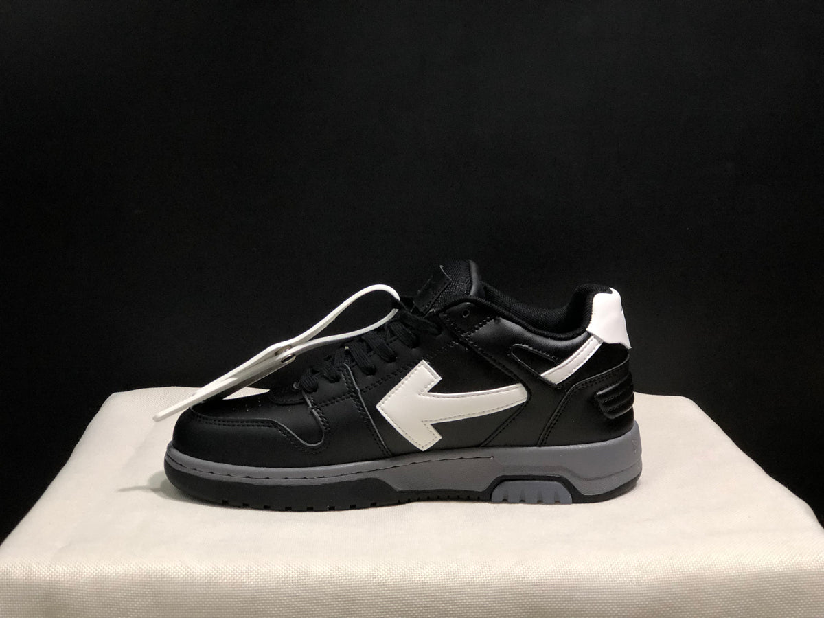 Lateral profile of a black low-top sneaker showing the white arrow detail, white heel accent, and gray outsole section.