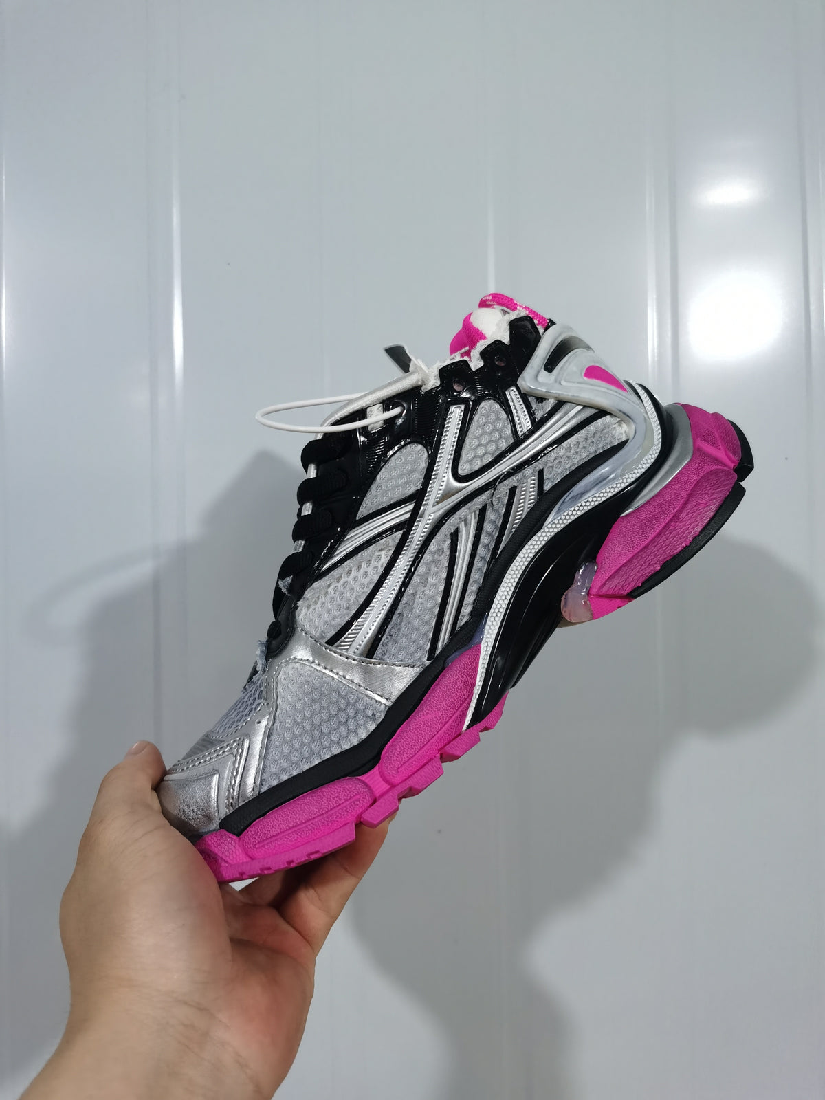 Side view showing the layered silver and black upper, mesh-textured panels, black laces, and fluorescent pink outsole.