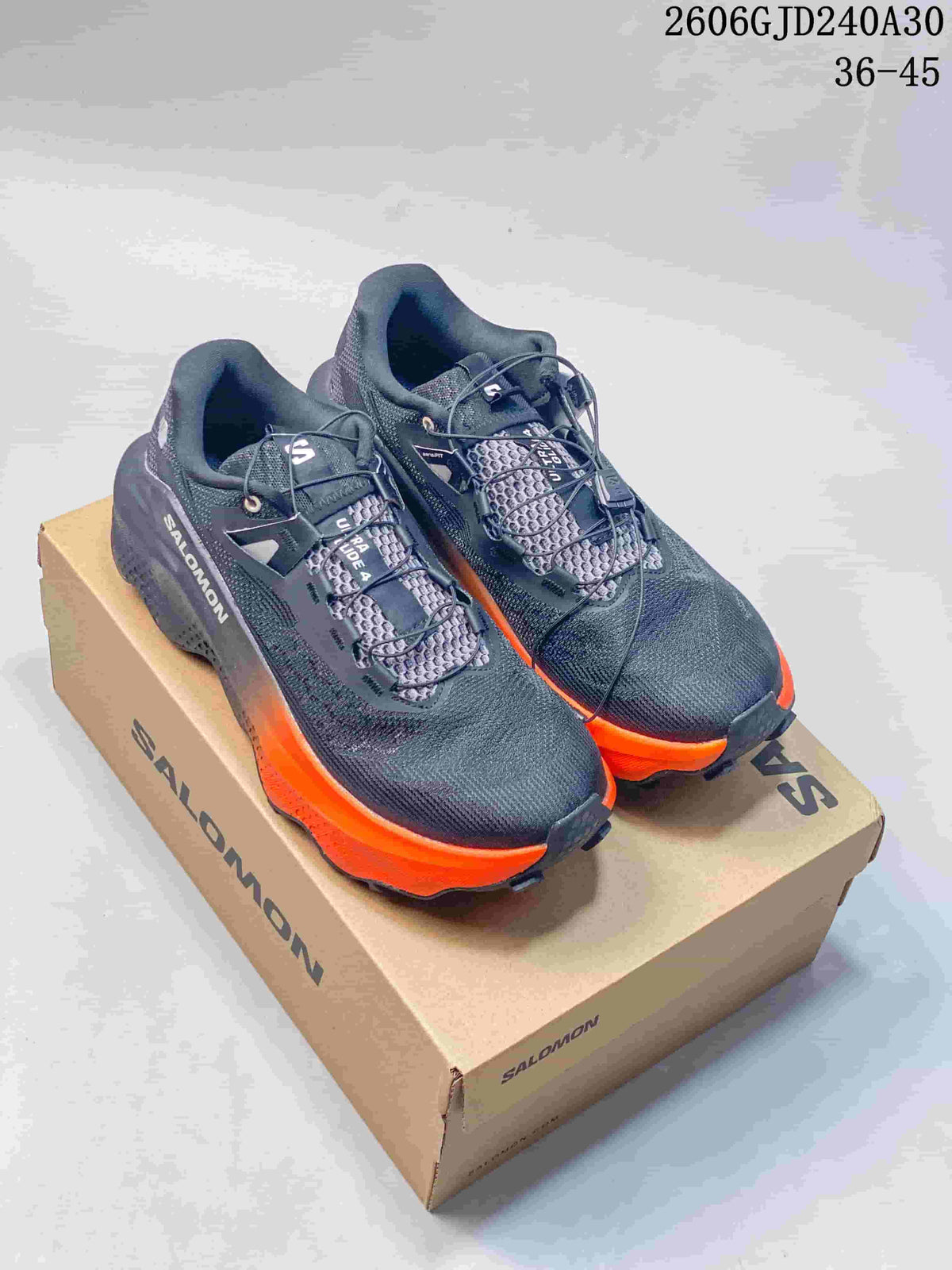Pair of charcoal Salomon Ultra Glide 4 shoes with bright orange outsole accents