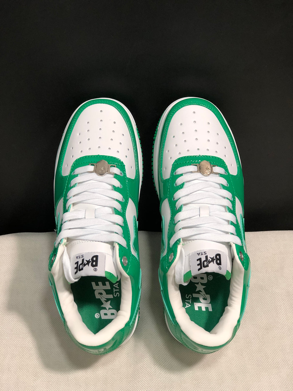Top-down view of the pair showing white laces, perforated toe panels, green overlays, and branded insoles.