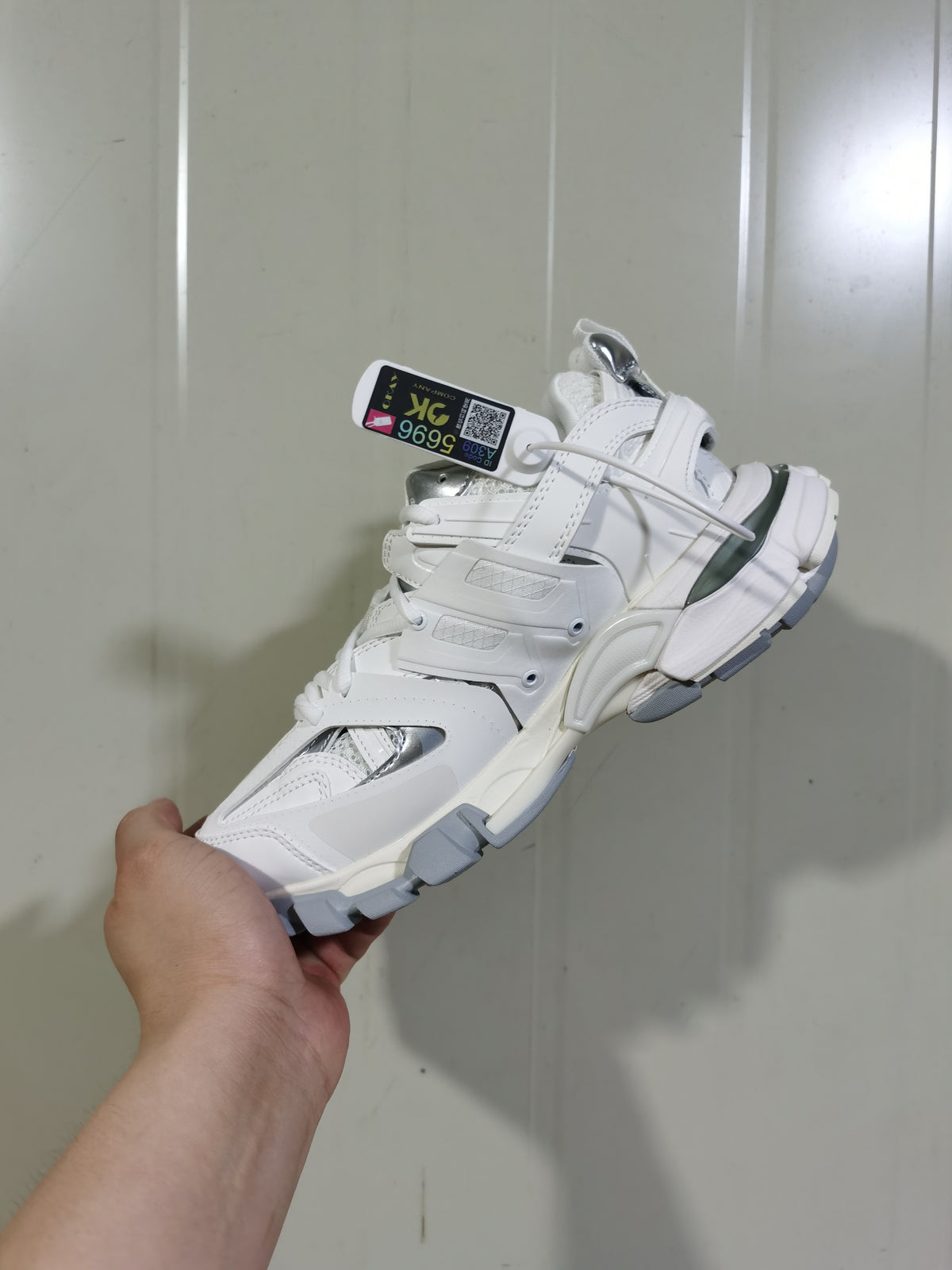 Angled view of the white and silver Track sneaker showing layered panels, mesh sections, reflective-look details, and gray outsole segments.