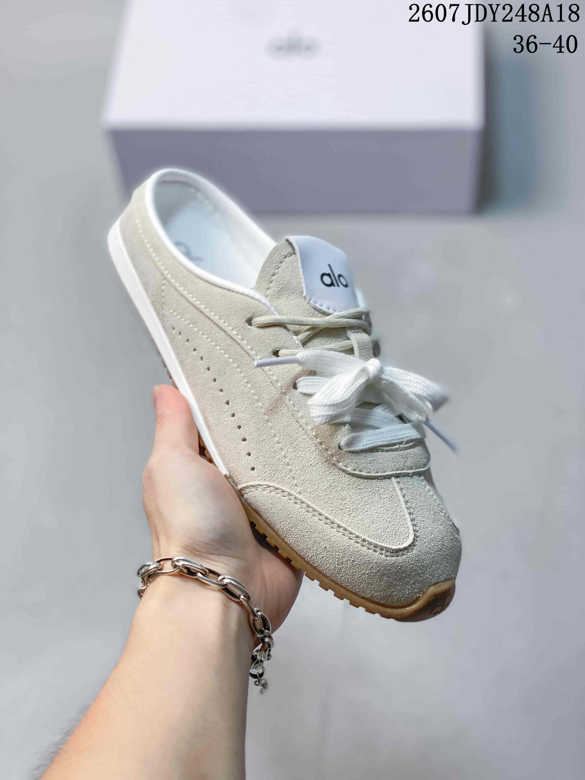 Angled side view of a cream Alo mule sneaker showing the lace-up front, perforated side detail, and open-back design.